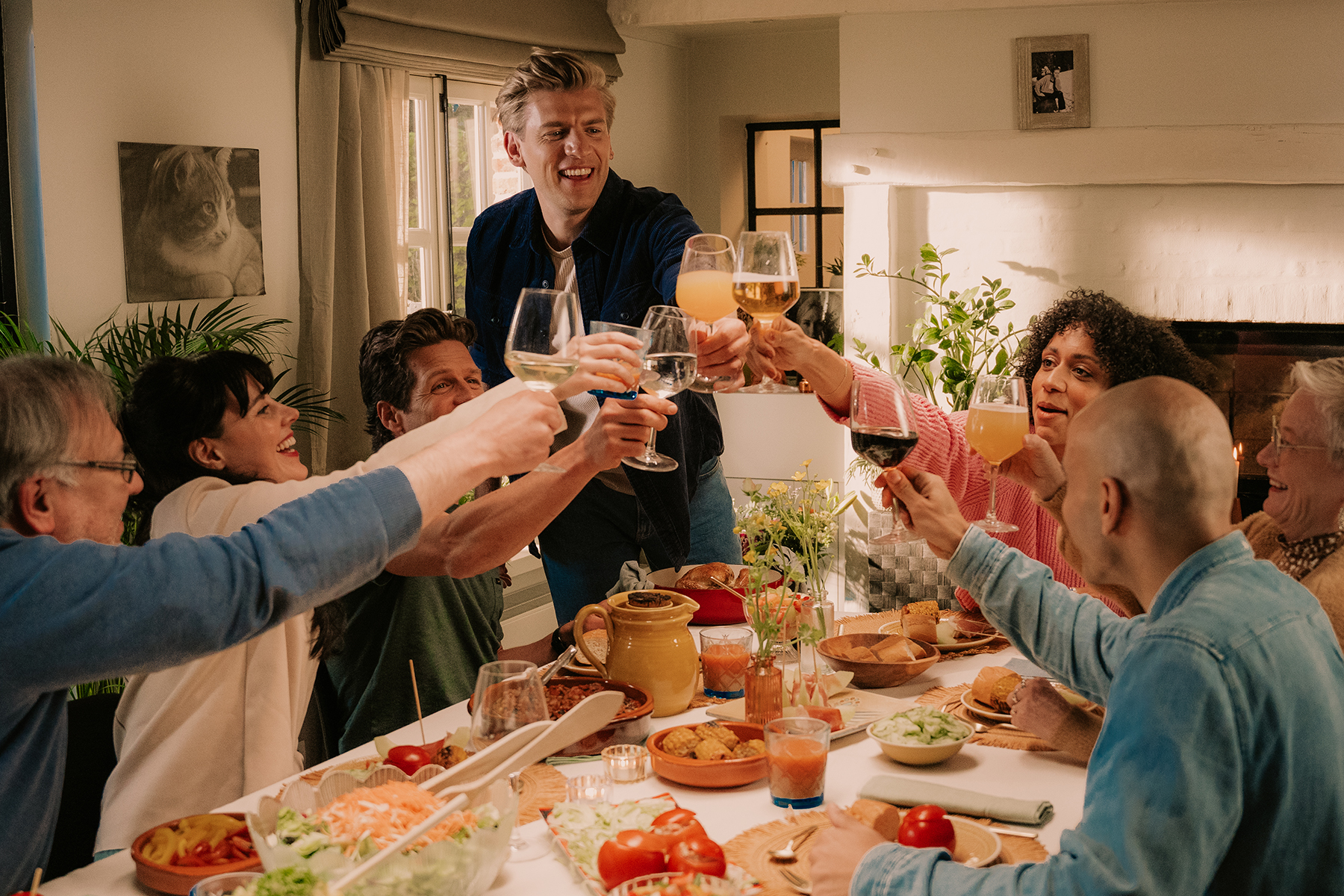 Groep vrienden klinken hun glazen aan tafel op een campagnefoto van De Nieuwe Levensgenieter